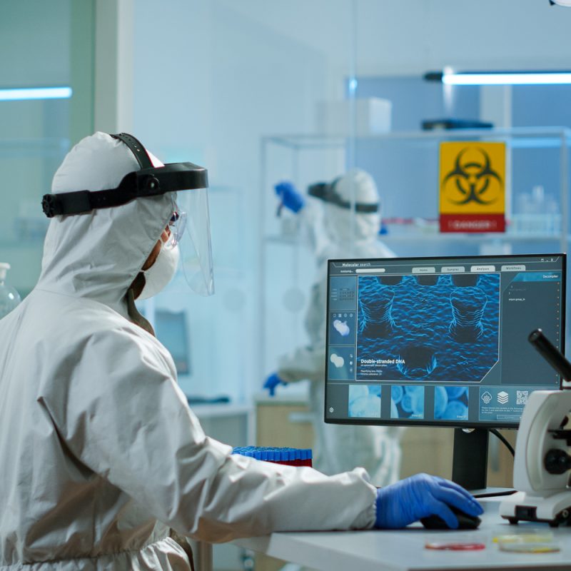 Medical scientist in ppe suit working with DNA scan image typing on pc in equipped laboratory. Examining vaccine evolution using high tech and chemistry tools for scientific research virus development